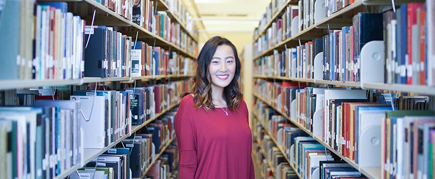 Student standing in rows of books at the library